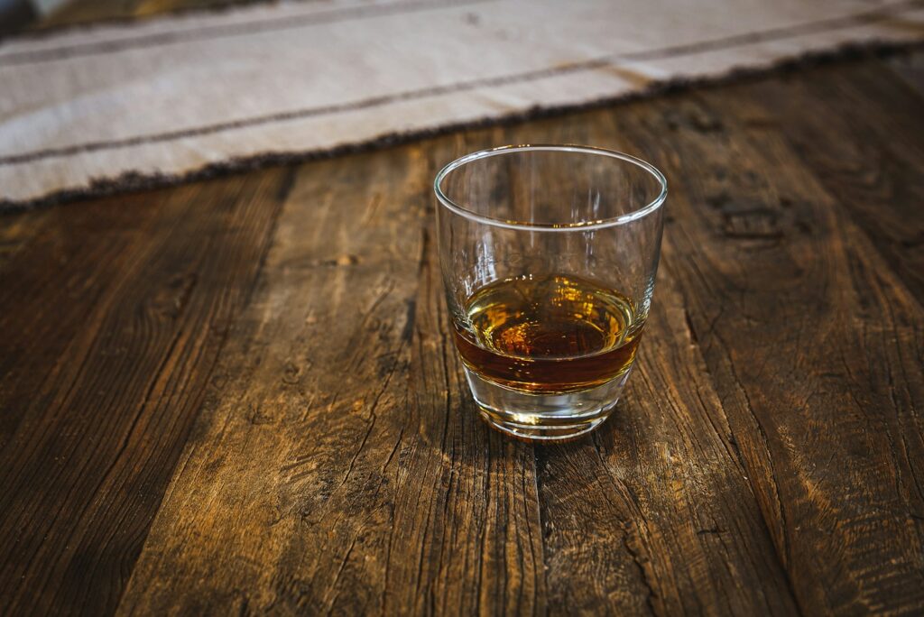 A single glass of whisky on a weathered oak table in warm light