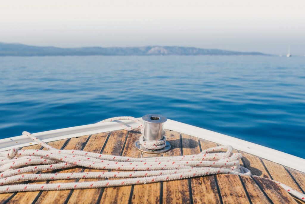 Yacht bow with coiled rope on a teak deck, looking out over calm blue sea